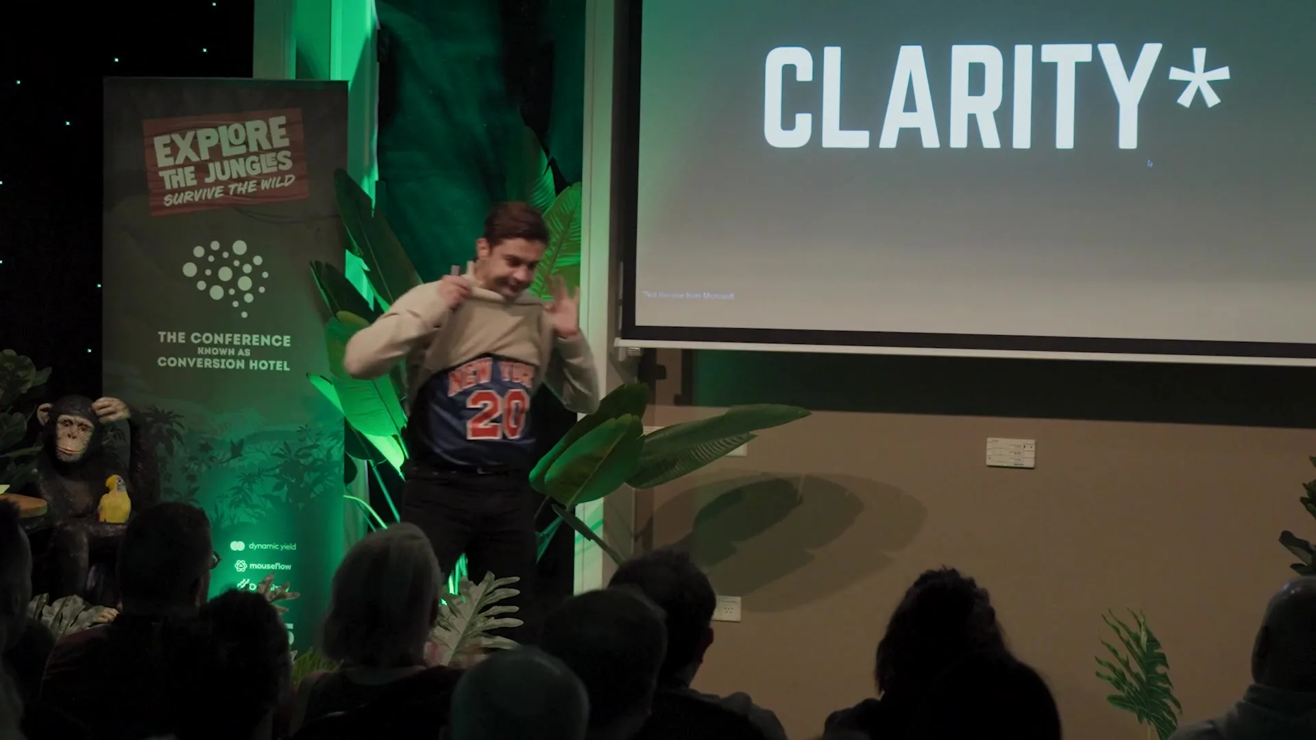 Sani on stage at Conversion Hotel 2025, lifting his sweater to show a blue and orange New York Knicks number 20 jersey underneath. The slide behind him reads CLARITY.